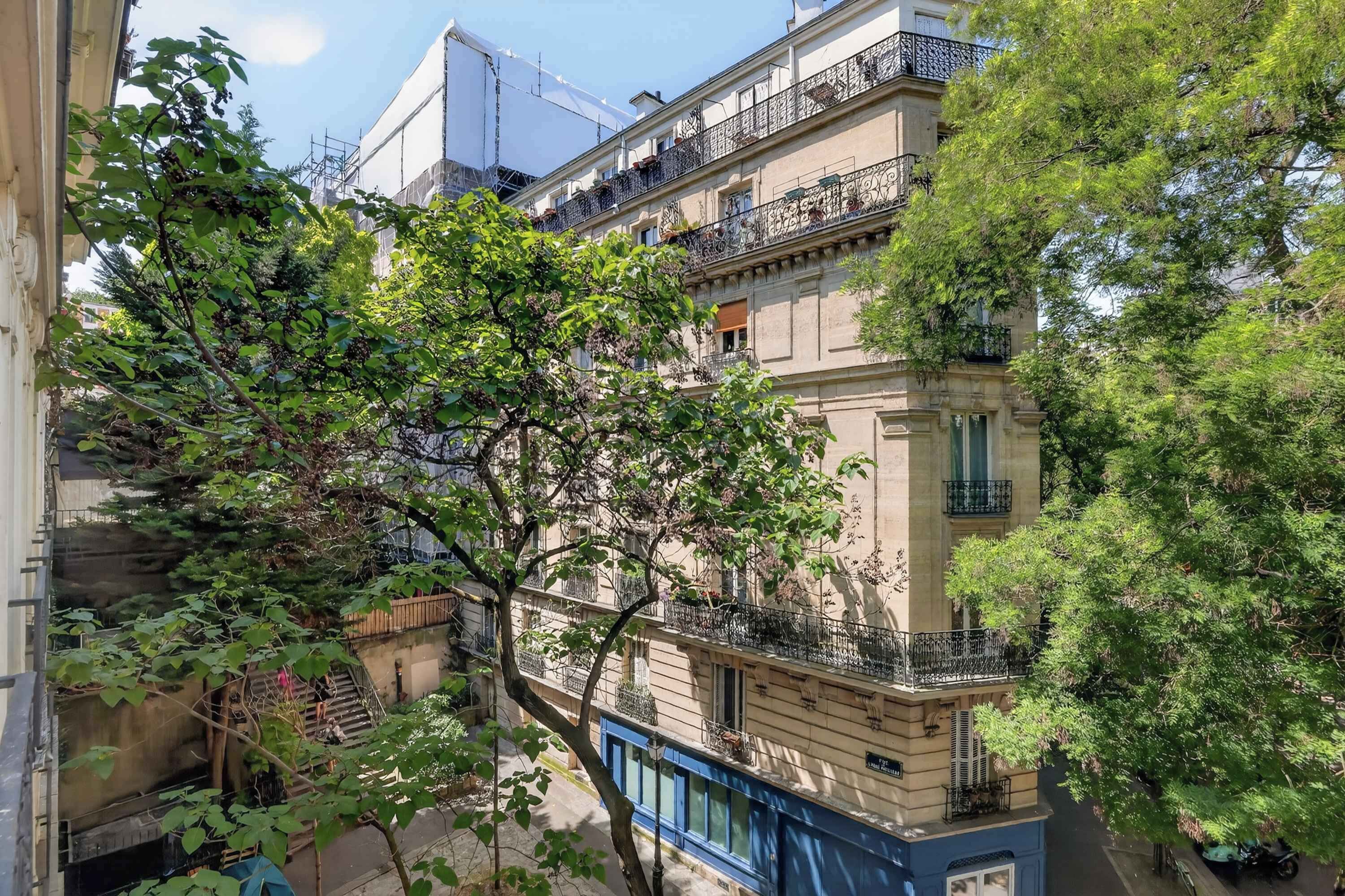 A multi-story building with balconies, a blue awning, and trees in the foreground.
