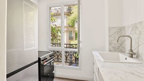Een compacte keuken met een ingebouwde oven, een spoelbak met een moderne kraan, en een groot raam met uitzicht op een balkon met een sierhekwerk.