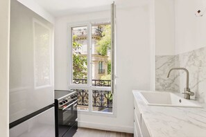 Eine kompakte Küche mit integriertem Backofen, einem Spülbecken mit modernem Wasserhahn und einem großen Fenster mit Blick auf einen Balkon mit schmiedeeisernem Geländer.