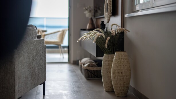 Un intérieur moderne avec un canapé, deux vases aux textures intéressantes et une vue sur la mer par une fenêtre.