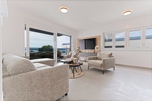 Ein modernes Wohnzimmer mit Sofa, Sesseln, Couchtisch und Fernseher.
