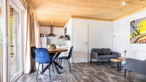 Una sala de estar moderna con techo de madera, un comedor con mesa de madera y sillas azules, un sofá gris y un cuadro en la pared.