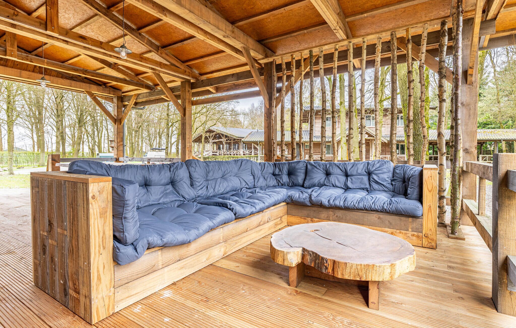 Een houten terras met een blauwe, bekleedde bank en een ronde houten tafel.