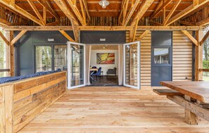Een houten interieur met een eethoek, een zithoek met kussens en een uitzicht door een glazen deur.
