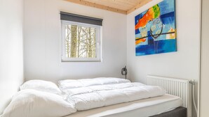 Un dormitorio con cama, ventana con vista a árboles y un cuadro en la pared.