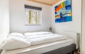 Ein Schlafzimmer mit einem Bett, einem Fenster mit Blick auf Bäume und einem Bild an der Wand.