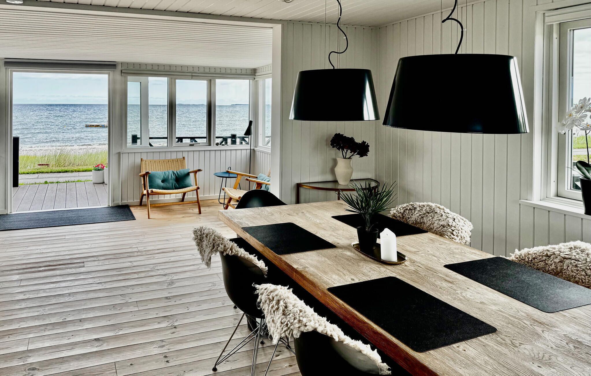 A dining area with a wooden table, black placemats, and a view of the sea through large windows.