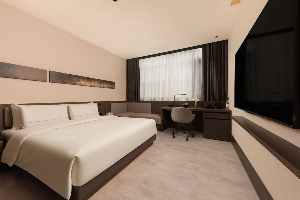 A hotel room with a large bed, a desk with a chair, a TV, and a window with curtains.