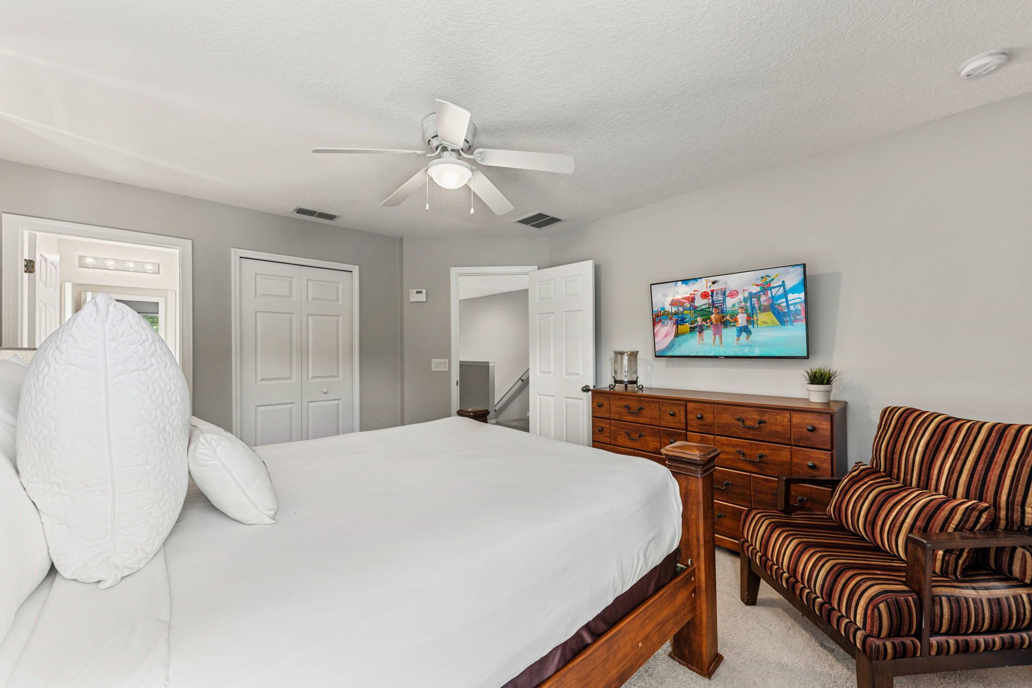 A bedroom with a bed, a dresser, a chair, a ceiling fan, and a television.