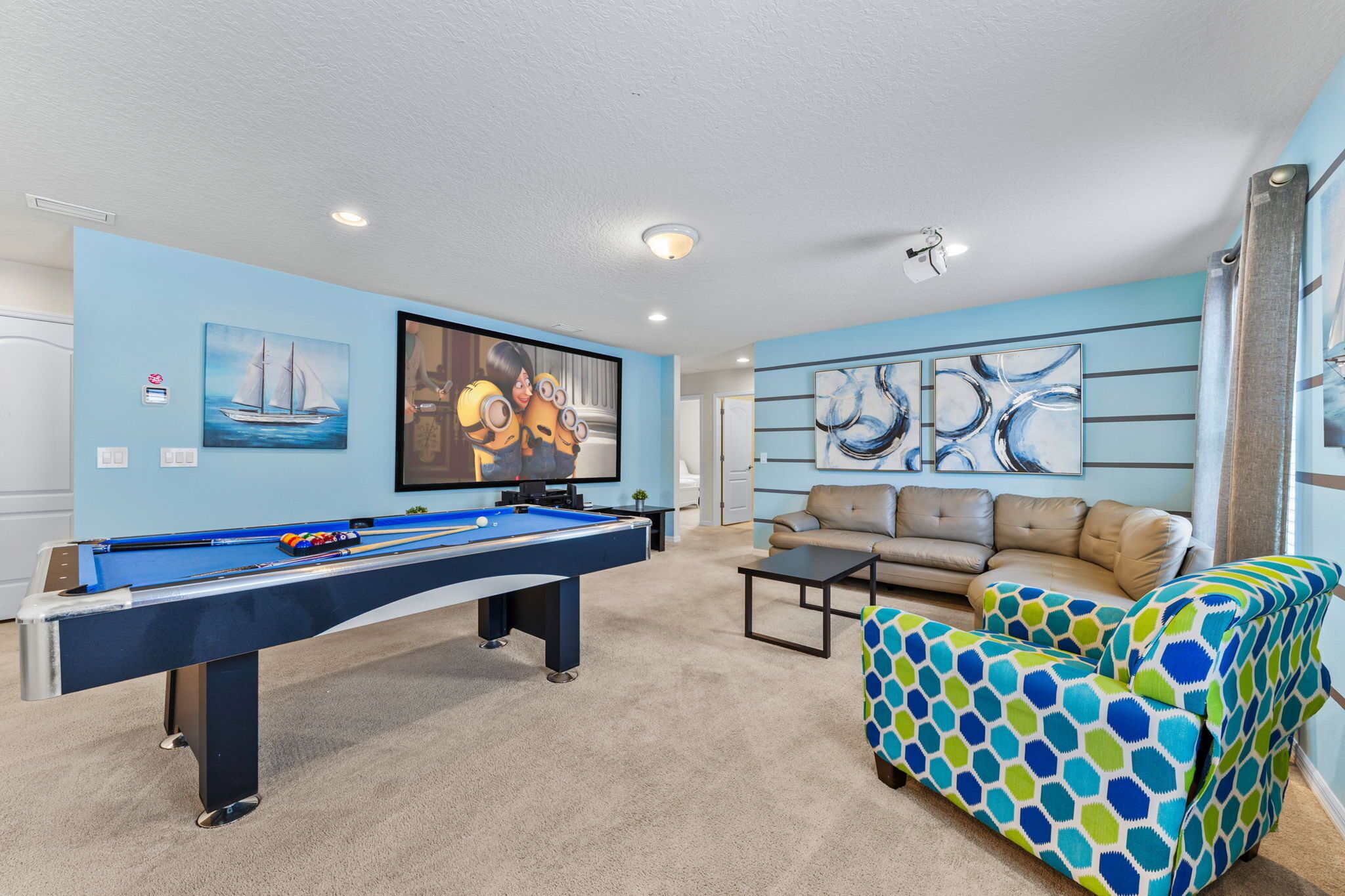 Een pooltafel, een bank en een kleurrijke stoel in een kamer met blauwe wanden en kunstwerken.