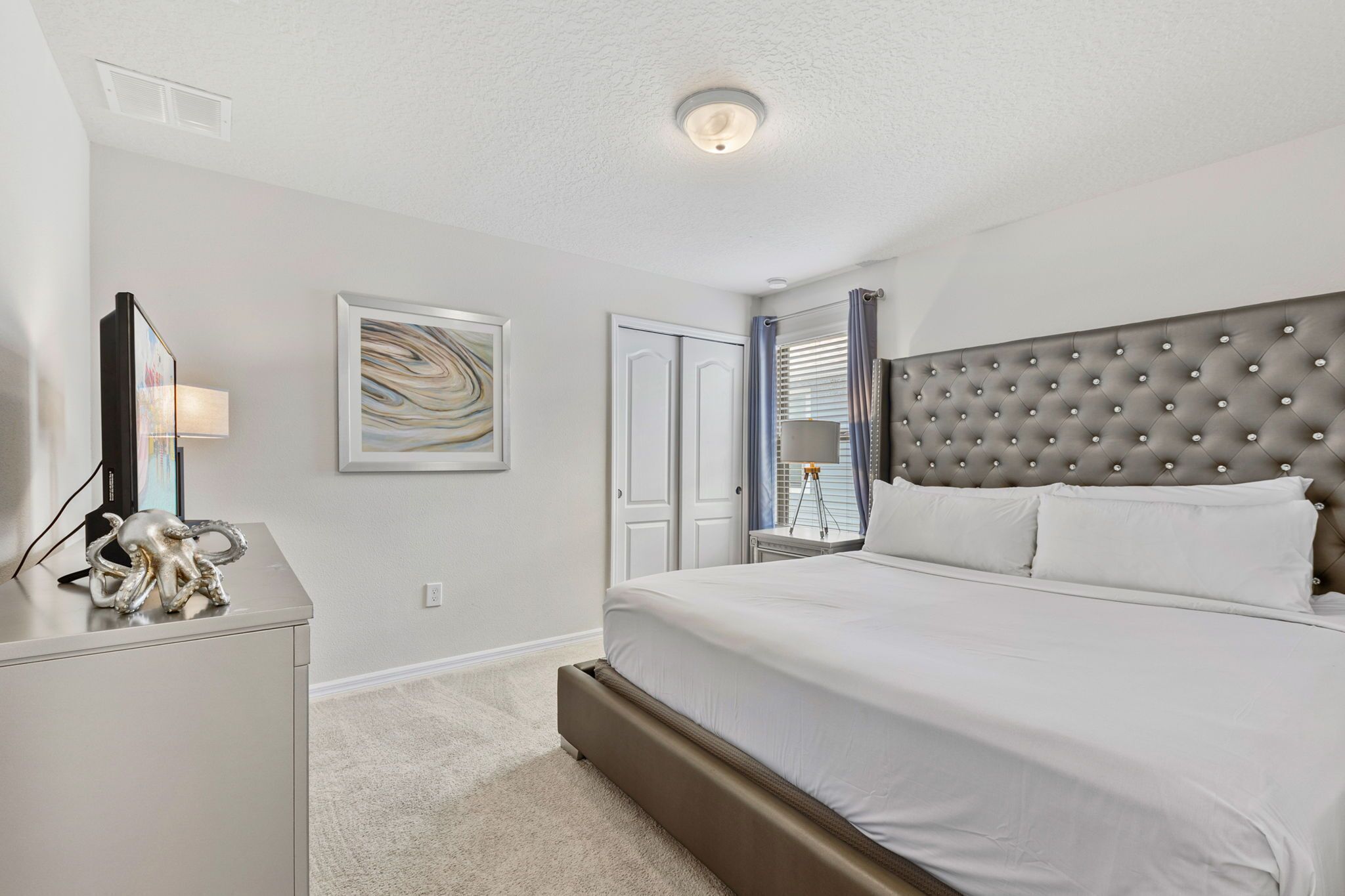 A bedroom with a large bed, a bedside table, a lamp, and a framed artwork on the wall.