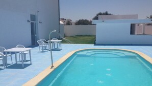 A swimming pool with a blue edge, surrounded by white chairs and a table. - Résidence Le Phare (Djerba Midun)