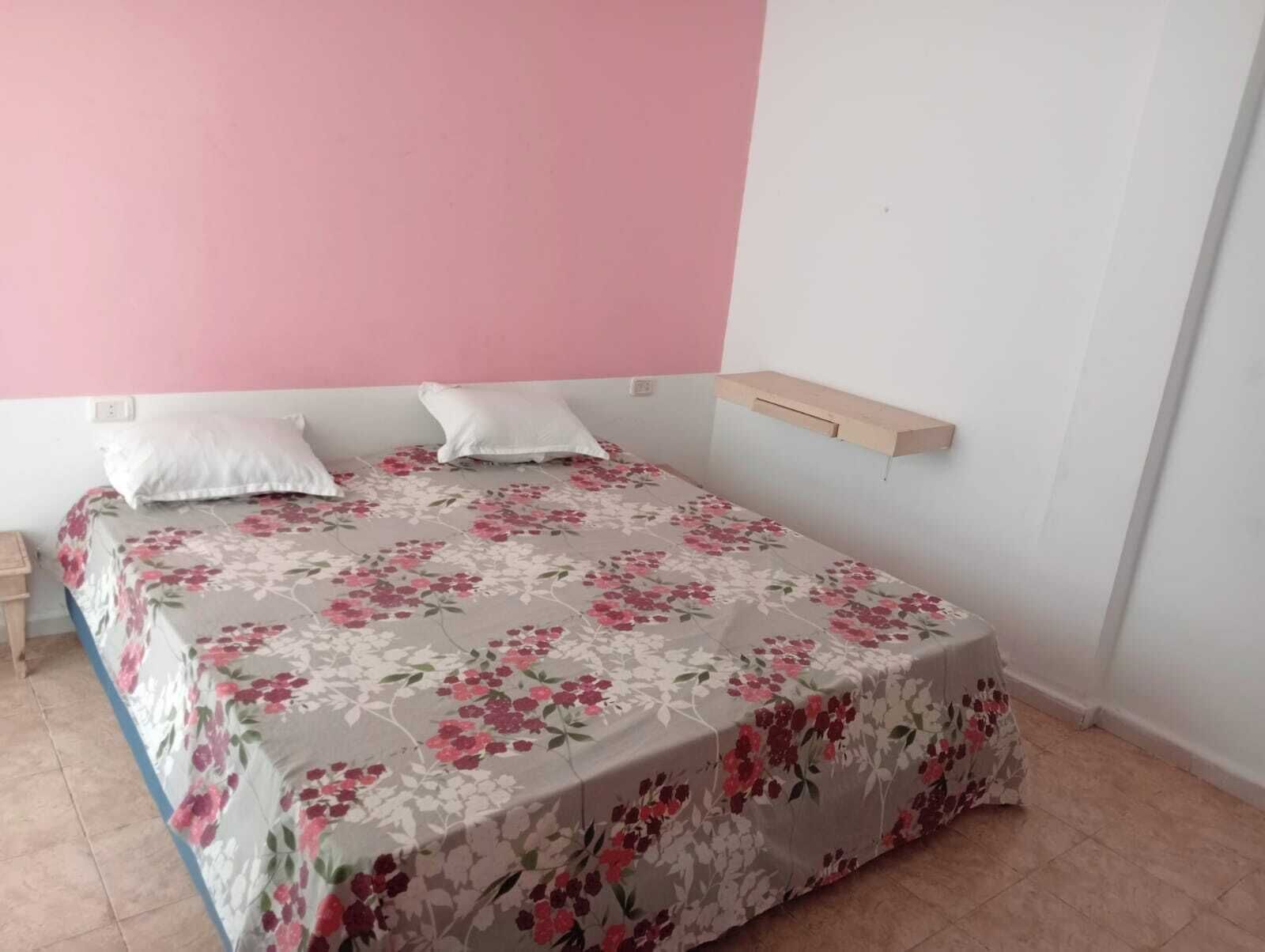 Un dormitorio con cama, dos almohadas, una mesita de noche y una estantería de madera.