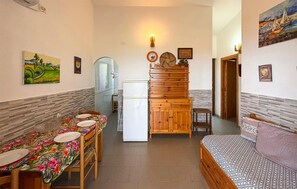 Eine kompakte Küche mit Esstisch, Kühlschrank und einem Bett mit gemusterten Textilien.