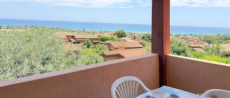 Ein Balkon mit Tisch für zwei Personen, mit Blick auf ein Küstendorf mit Häusern mit Terrakotta-Dächern und blauem Himmel.