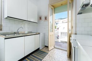 A kitchen with white cabinets, a stainless steel sink, a dish rack, and a patterned rug. - Apartment 'Casa Nerea' with Balcony and Wi-Fi (Dorgali)