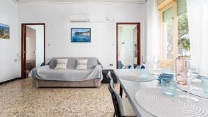 A room with a bed, a dining table with chairs, a window with curtains, and a wall-mounted air conditioner. - Apartment 'Casa Nerea' with Balcony and Wi-Fi (Dorgali)
