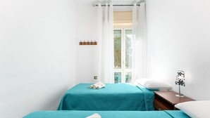 A room with two beds, a nightstand, a lamp, and a window with curtains. - Apartment 'Casa Nerea' with Balcony and Wi-Fi (Dorgali)