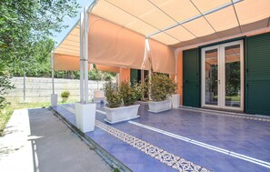Ein überdachter Patio-Bereich mit Kübelpflanzen, Fliesenboden und einer grünen Tür.