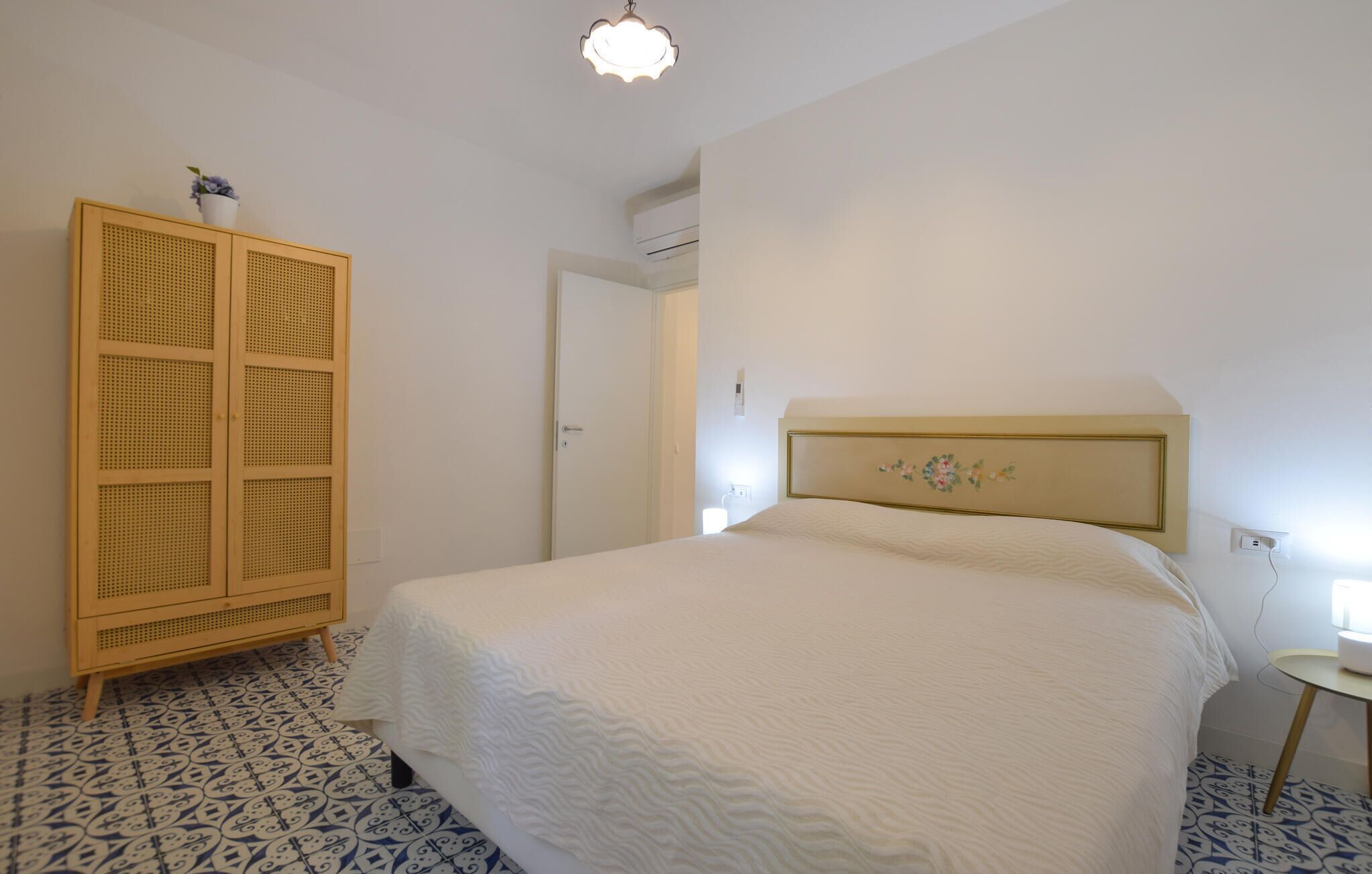 Une chambre à coucher comprenant un lit, une armoire, une table de chevet et un climatiseur fixé au mur.