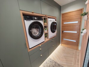 Ein Waschraum mit zwei Waschmaschinen, einer Holztür und einem kleinen Regal mit Pflanzen.