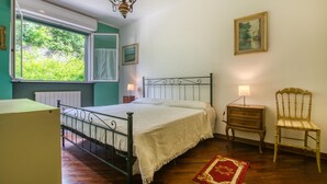 A bedroom with a bed, a chair, a nightstand, a window with curtains, a radiator, and a painting on the wall. - 2 bedroom lovely apartment in Genova (Genova)