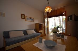 Ein gemütliches Wohnzimmer mit einer Couch, einem Esstisch mit Schüssel und Blumenvase sowie einem Holzschrank.