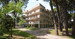 Ein mehrgeschossiges Wohnhaus mit Balkonen, umgeben von Bäumen und einem Kiesweg.