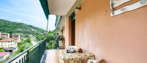 A balcony with a table and chairs, a view of a hillside town, and a railing.