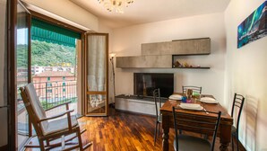 Ein Essbereich mit einem Holztisch, Stühlen, einem Fernseher und einem Balkon mit Blick auf Gebäude.