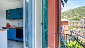 Ein Balkon mit Blick auf eine Hügellandschaft, eine Küche mit blauen Schränken und eine Glastür zum Verschieben.