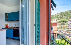 Un balcon donnant sur une colline, une cuisine avec des meubles bleus et une porte-fenêtre coulissante.