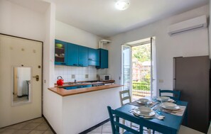 Une cuisine compacte avec des meubles de couleur turquoise, une bouilloire rouge et un coin repas avec une table dressée pour quatre personnes.