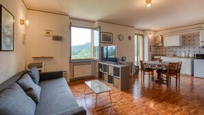Un espacio habitable compacto con sofá, mesa de comedor, zona de cocina y un ventanal con vistas.