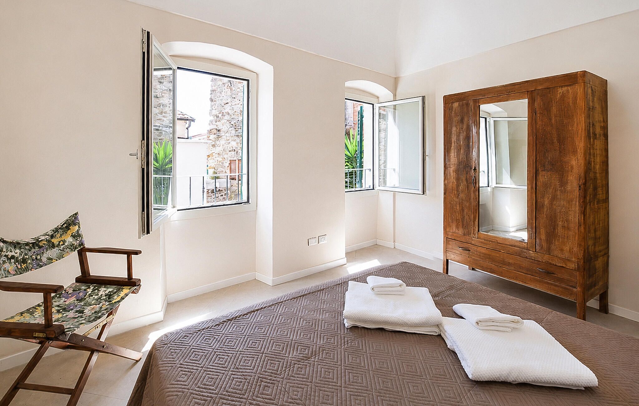 Un dormitorio con cama, armario de madera, una silla y ventana con vistas a vegetación.