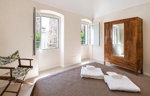 Ein Schlafzimmer mit einem Bett, einem Holzschrank, einem Stuhl und einem Fenster mit Blick auf Grünfläche.