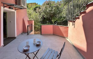 Eine Terrasse im Freien mit Tisch und Stühlen, einem Metallgeländer und einer Tür zu einem Innenbereich.