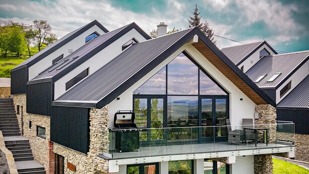 A modern house with a stone facade, large windows, and a balcony.