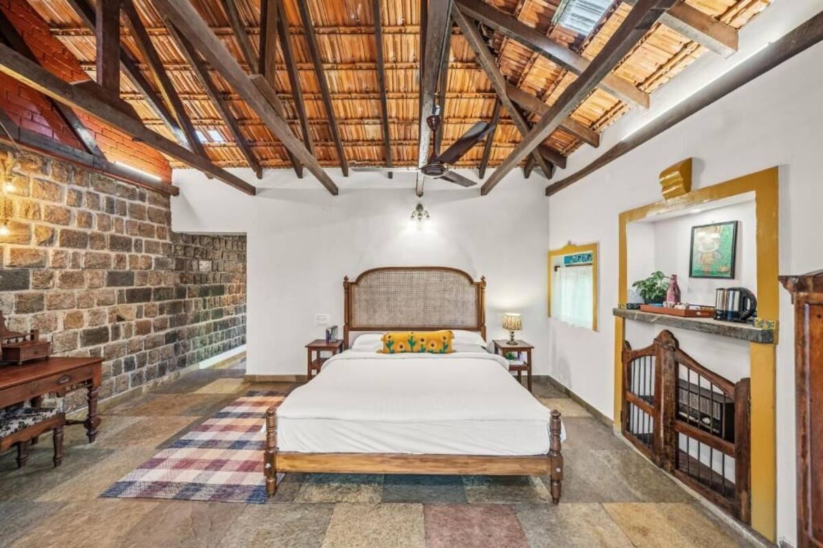 A bedroom with a stone wall, a wooden bed, a ceiling fan, and a nightstand with a lamp.