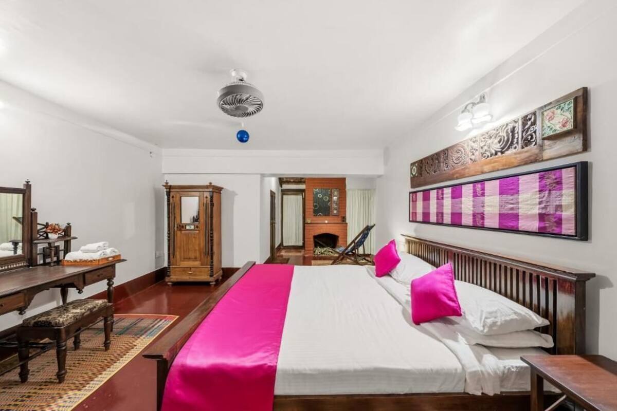 A bedroom with a bed, wooden headboard, a desk, a chair, a fireplace, and a ceiling fan.