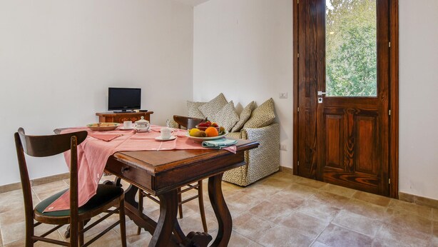 A dining area with a table set for two, a television, and a sofa with patterned cushions. - Cozy home in Caltagirone with WiFi (Caltagirone)