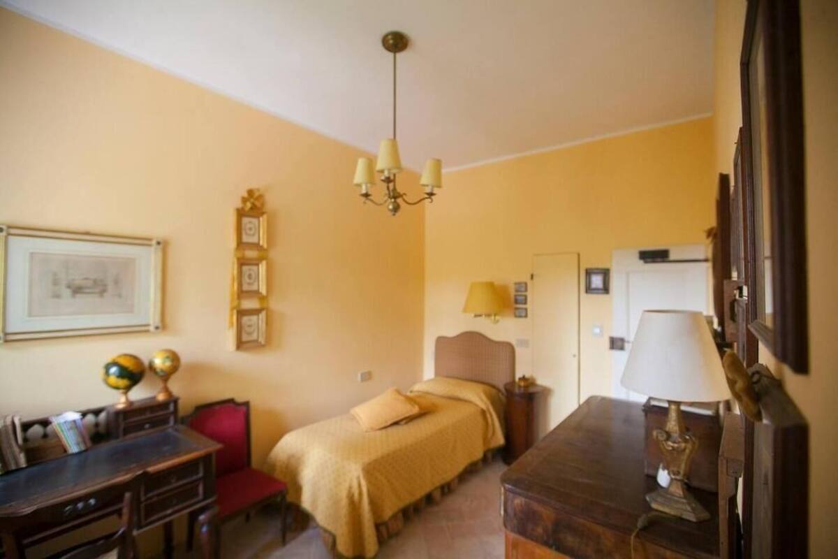 Una habitación con una cama, un escritorio, una silla, una lámpara, un reloj y un cuadro en la pared.