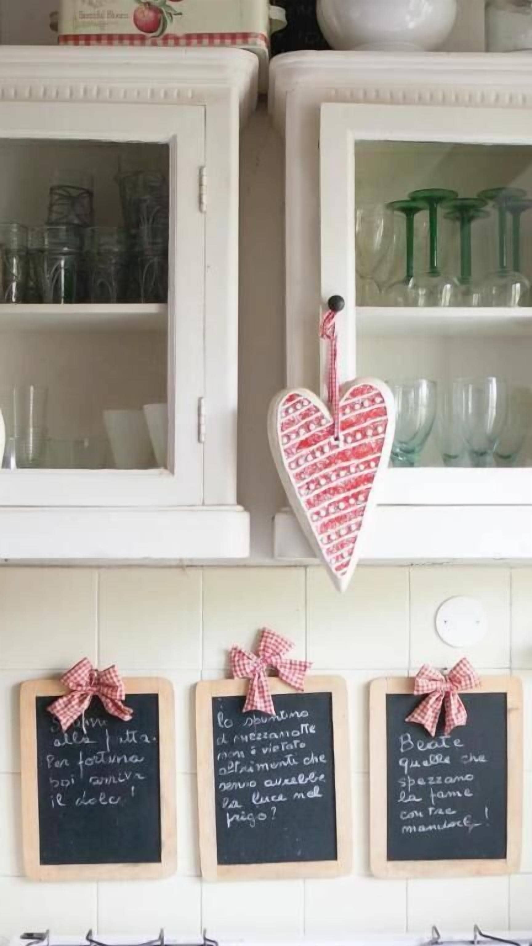A kitchen with white cabinets, glassware, and chalkboards with handwritten notes.