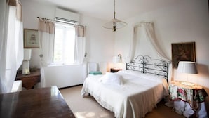 A bedroom with a bed, bedside tables, a window with curtains, a hanging light fixture, and a painting on the wall. - Casale novilara (Novilara)