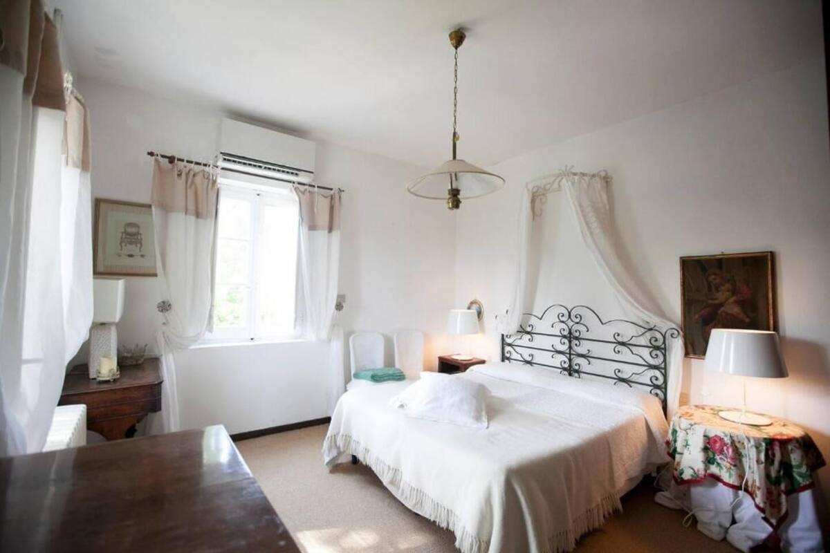 Un dormitorio con cama, mesitas de noche, una ventana con cortinas, una lámpara colgante y un cuadro en la pared.