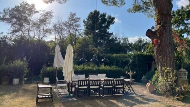 An outdoor patio with a table and chairs, surrounded by trees and greenery. - Casale novilara (Novilara)