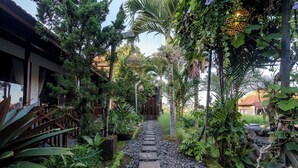A stone pathway leading to a wooden structure surrounded by lush greenery and a hanging light fixture. - Kasubatu (City)