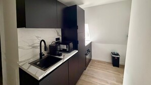 A modern kitchen with dark cabinetry, a marble countertop, and a built-in microwave. - Cosy studio - Hypercentre - Renovated - Calm and chic (Thonon-les-Bains)