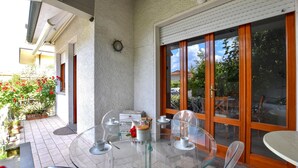 A glass table with white cups and saucers, a wooden door with glass panels, and a view of a garden with red flowers. - 2 bedroom stunning home in Lido di Camaiore (Lido di Camaiore)