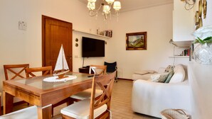 A living room with a wooden dining table, chairs, a sofa, a TV, and a chandelier. - 2 bedroom stunning home in Lido di Camaiore (Lido di Camaiore)